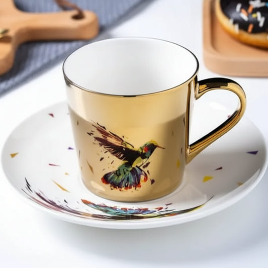 Gold mug with a bird design on a white saucer, placed on a light surface.
